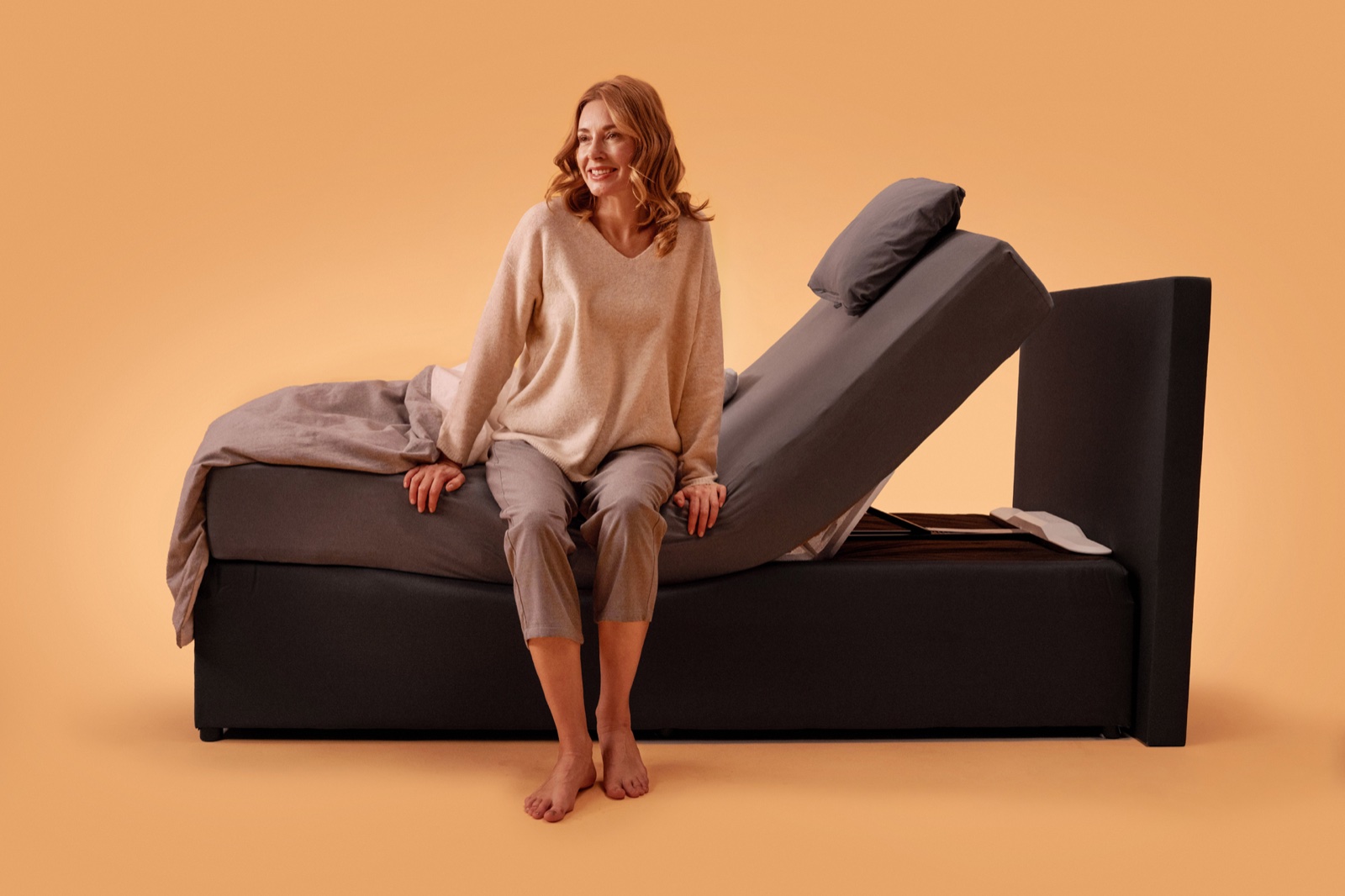 Donna seduta sul bordo del letto, con il materasso sollevato dal CosyLift alle spalle